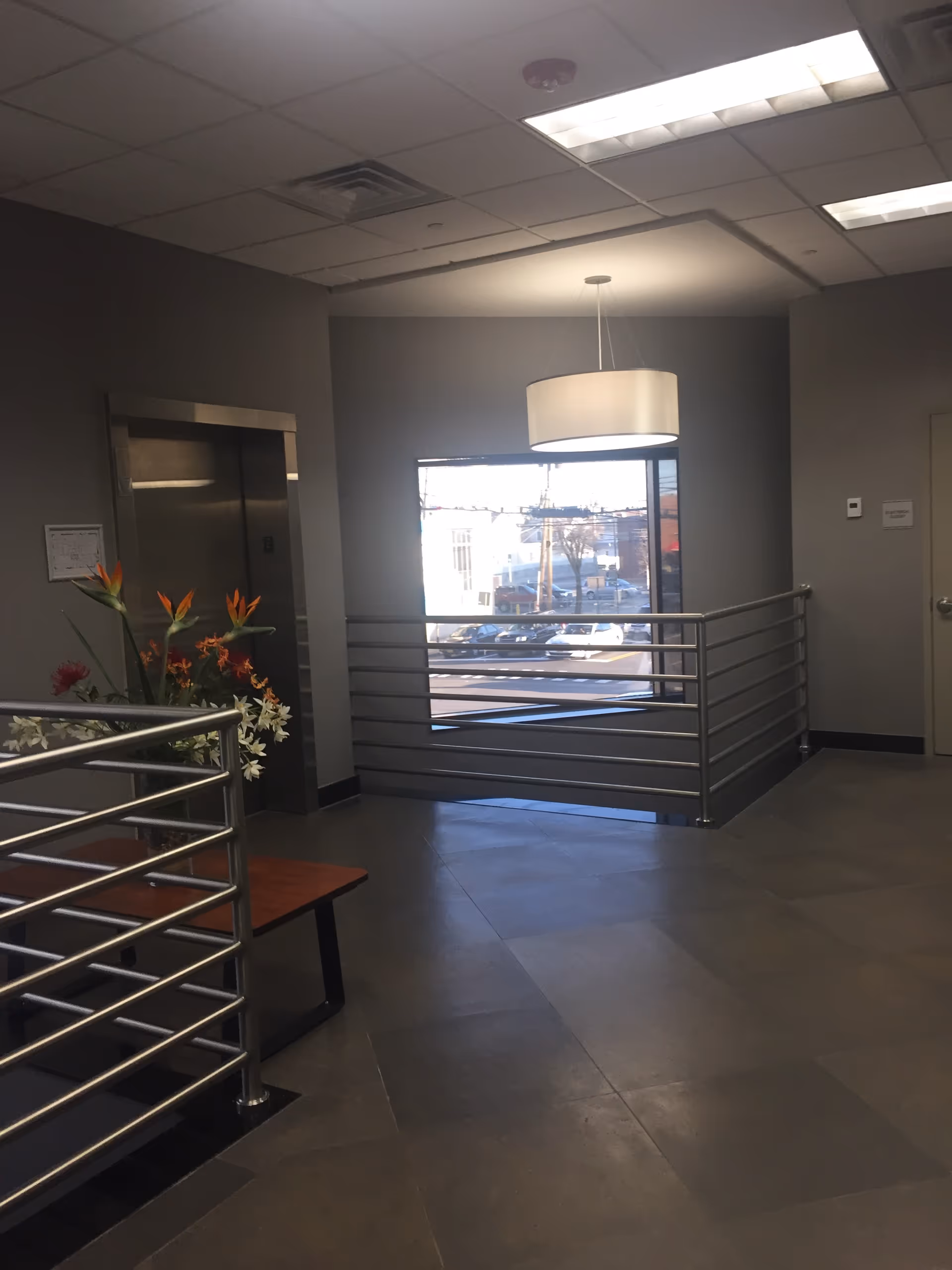 Modern interior lobby with metal railings, bench, and a large window overlooking outdoors.