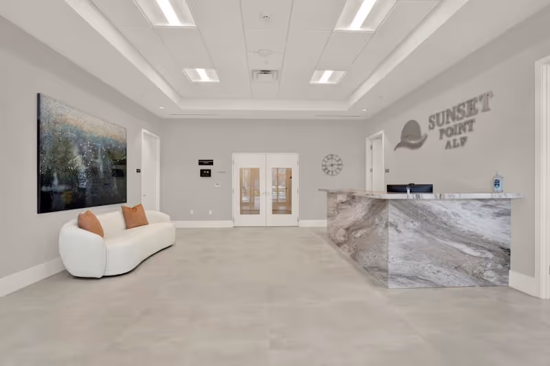 Modern lobby with marble reception desk, a white curved sofa, and Sunset Point ALF signage.