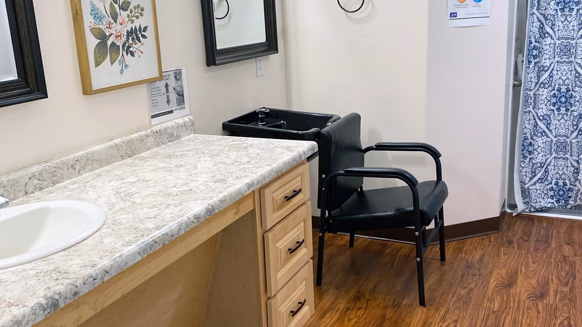 Marble countertop with sink, drawers, chair, and blue shower curtain in a bright bathroom.