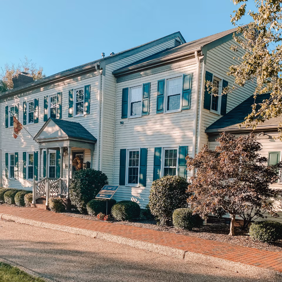 Two-story white senior living building with teal shutters and manicured landscaping along a brick sidewalk