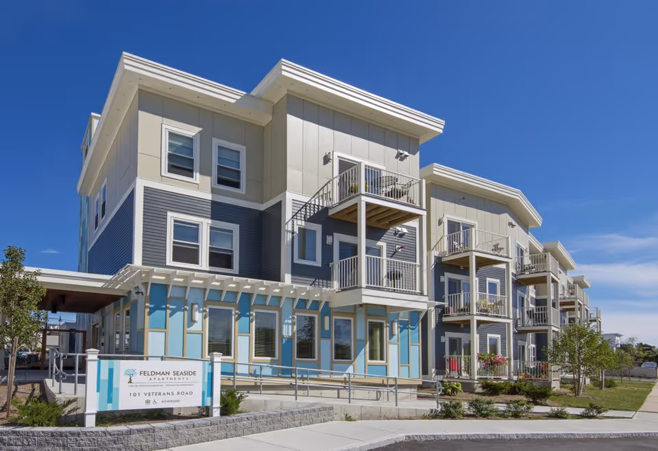 Multi-story Feldman Seaside Apartments building with balconies, modern facade, exterior signage, and welcoming entrance.