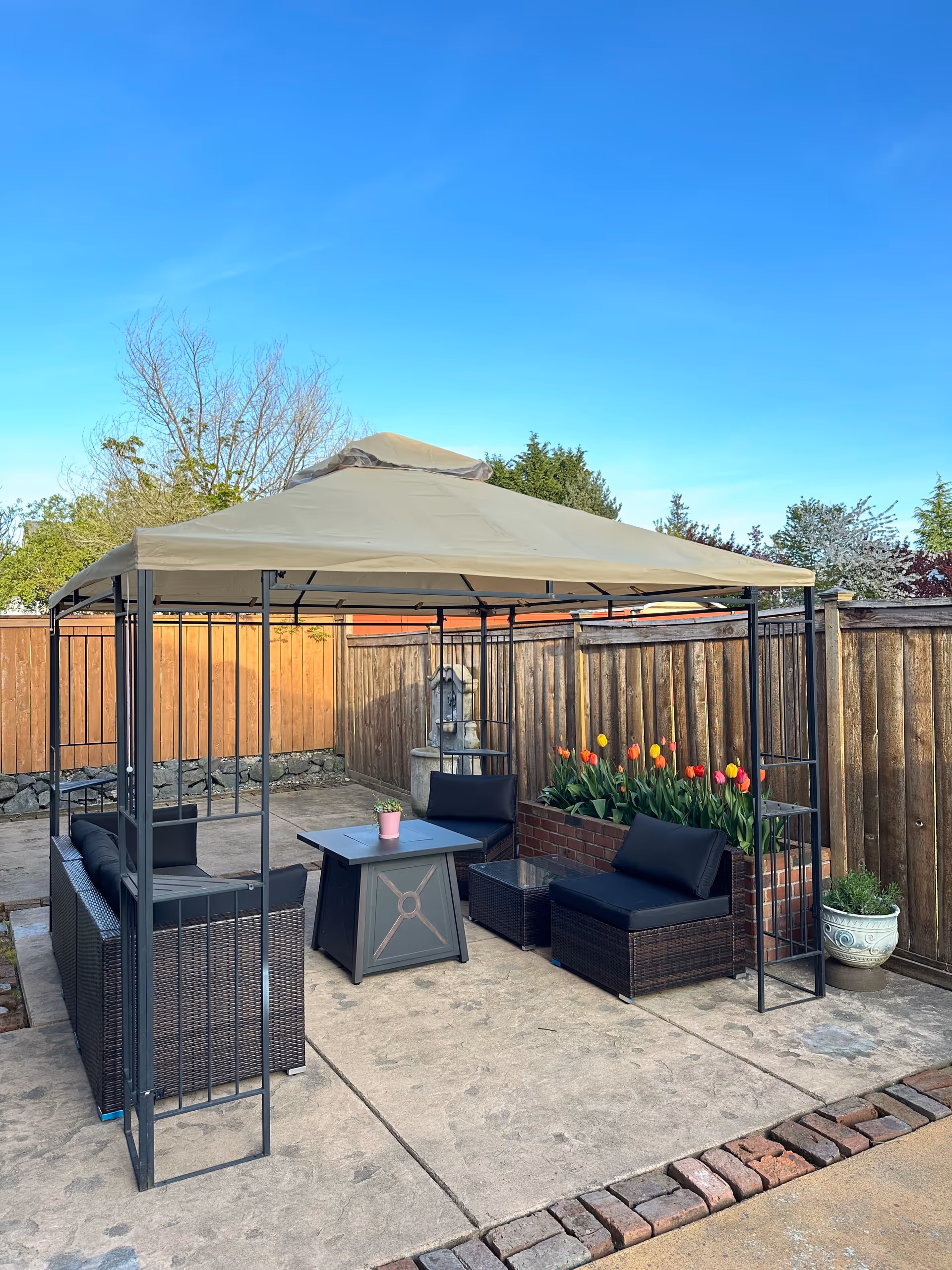 Outdoor seating area under a beige canopy with wicker furniture and flowers.