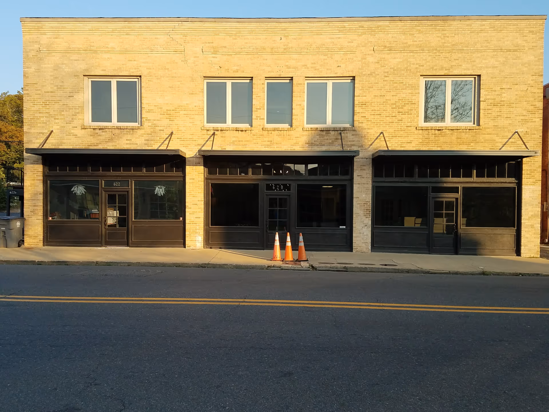 Brick storefront building with three black entrances and large display windows along a sidewalk.