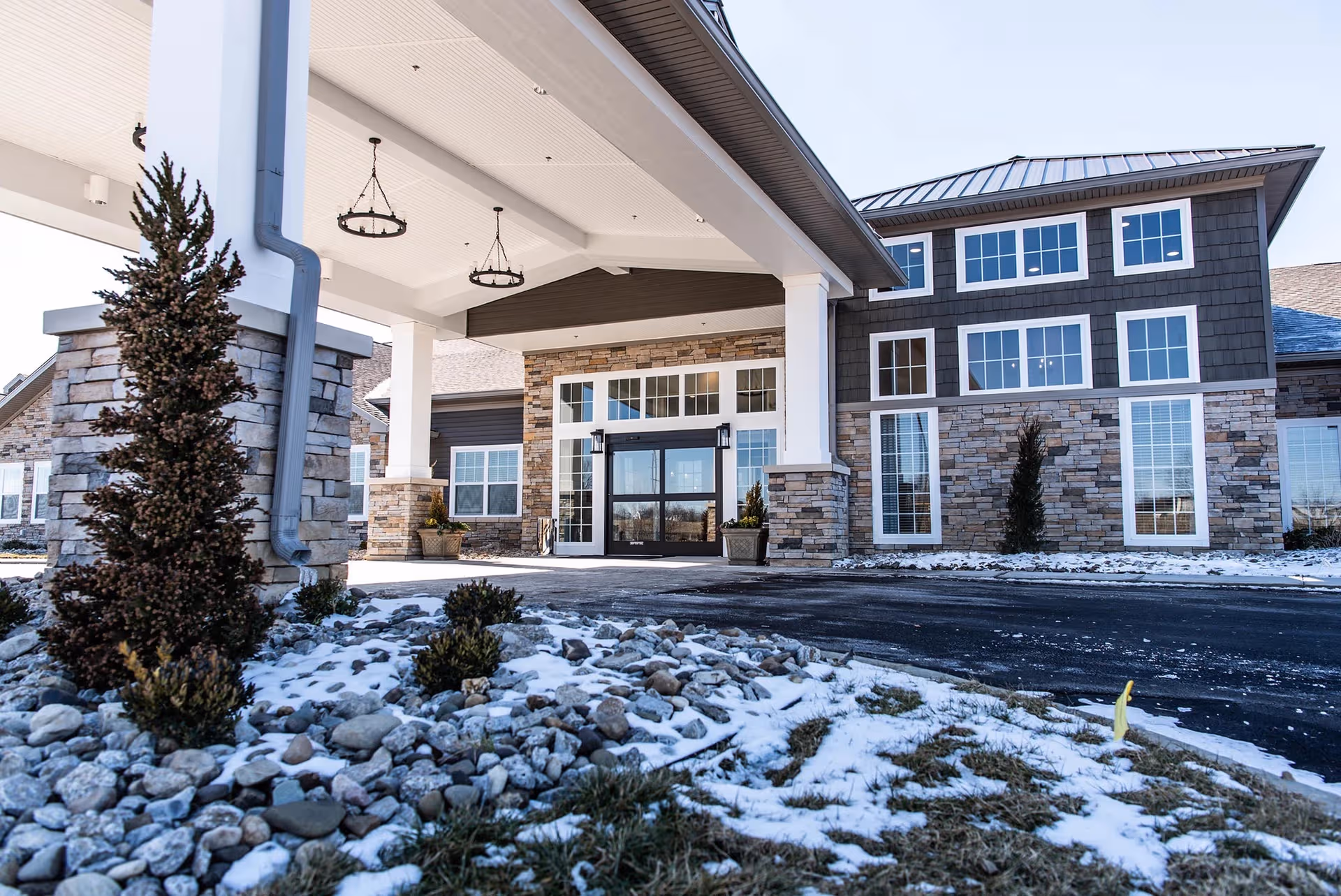 Exterior entrance of Charter Senior Living of Linden with stone columns and snow.
