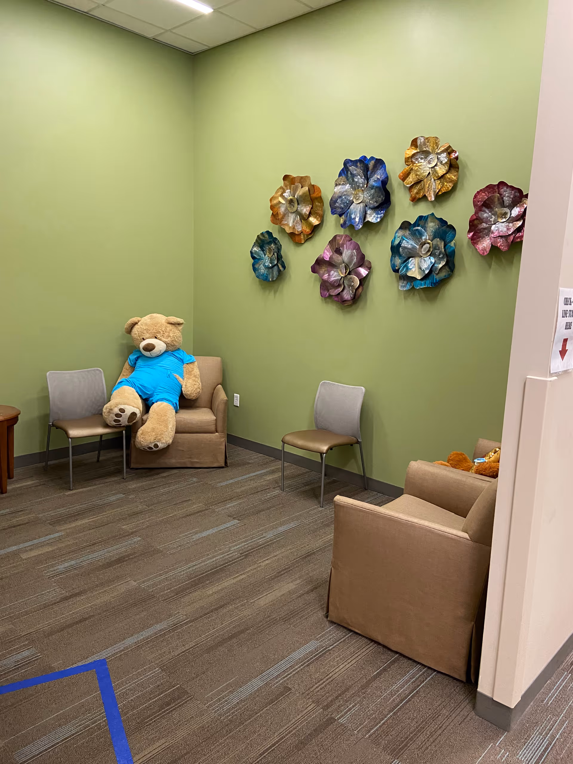 Bright green lounge with a teddy bear on a chair and colorful wall decor.