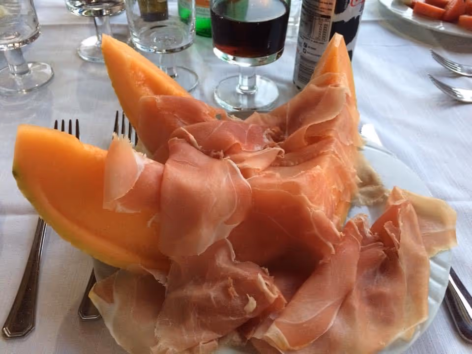 Overhead view of a plate with melon slices and prosciutto on a dining table.
