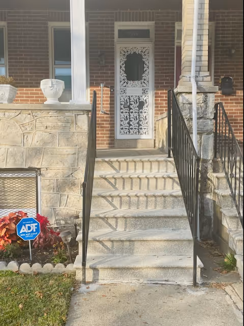 Brick building entrance with stone steps, black metal railings, and an ornate white door.