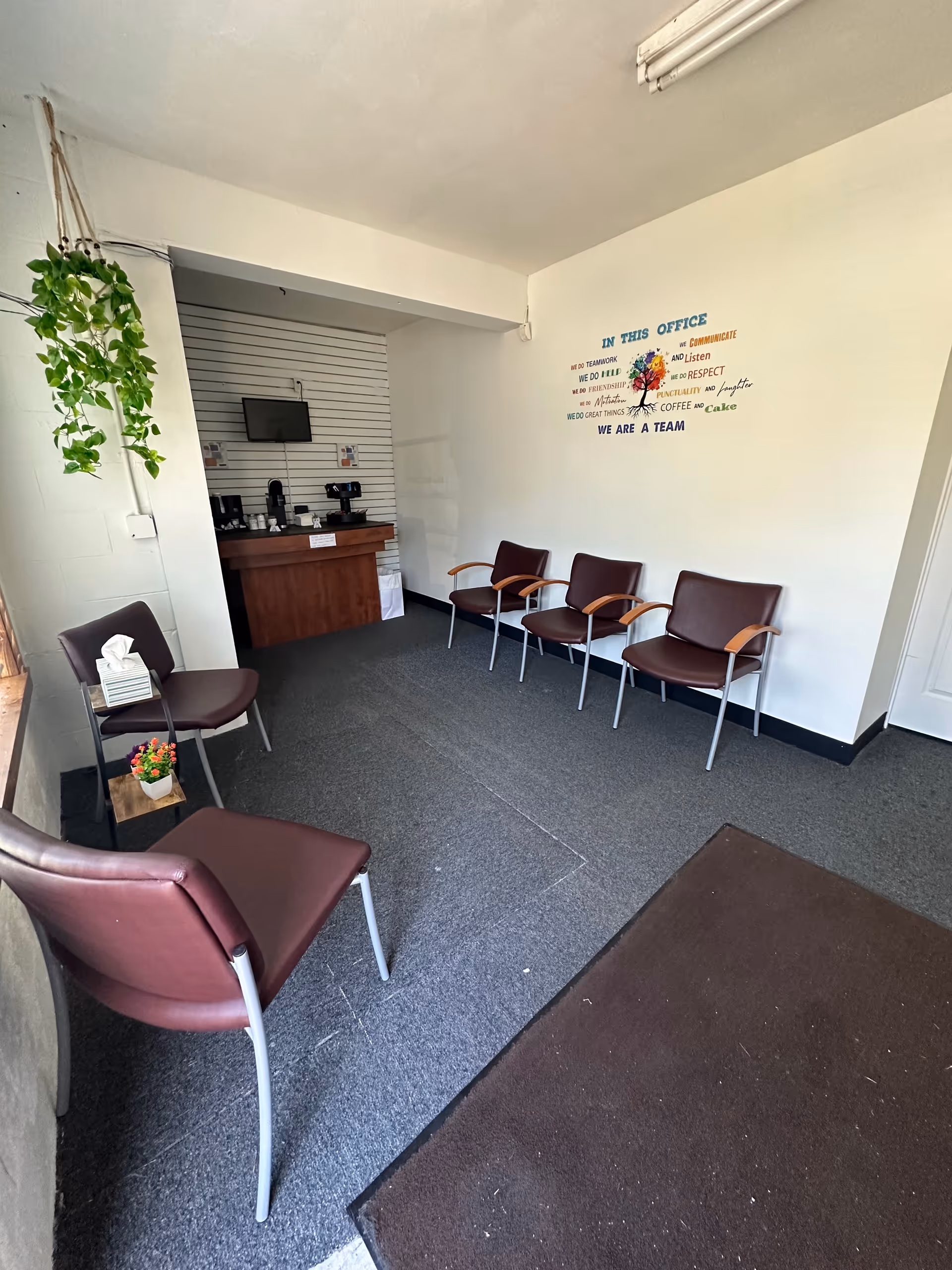 Small waiting area with brown chairs, a desk, and a hanging plant.