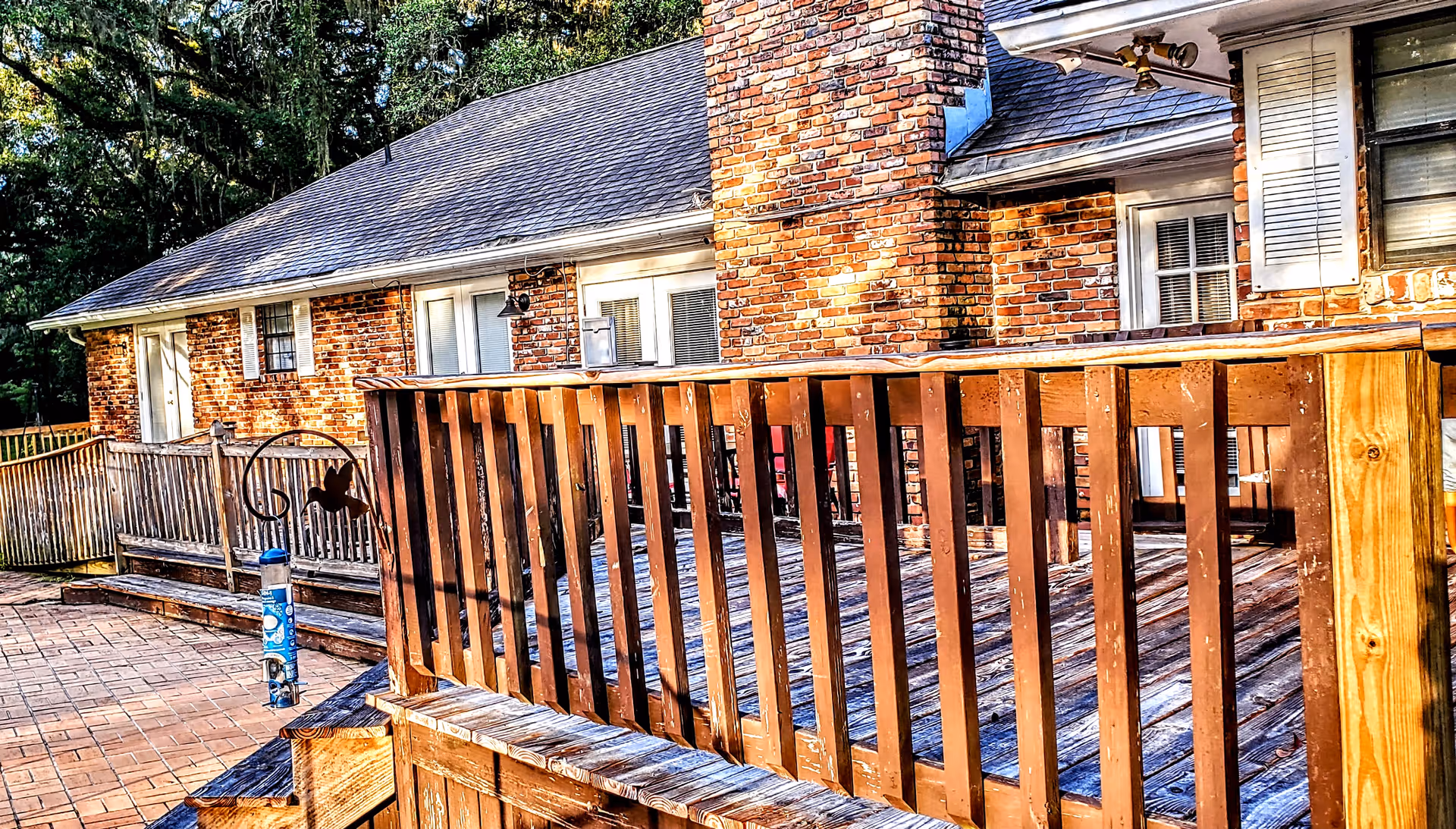 Brick residential building with wooden deck railing and surrounding trees outdoors.