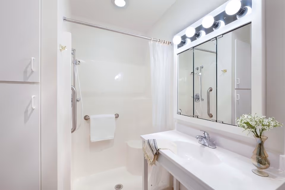 Bright white bathroom with shower, sink, mirror, and towel bar.
