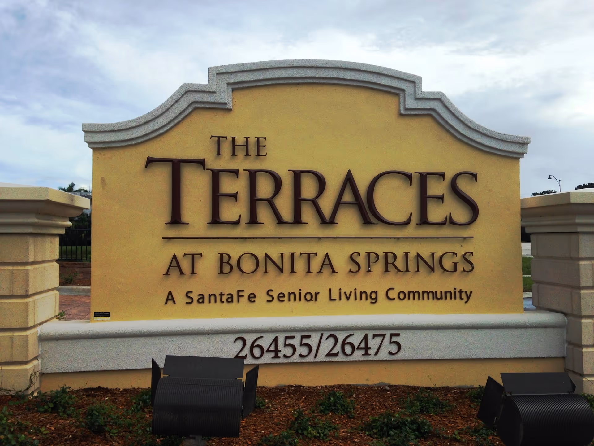 Large entrance stone sign reading 'The Terraces at Bonita Springs, A SantaFe Senior Living Community' with address numbers below.