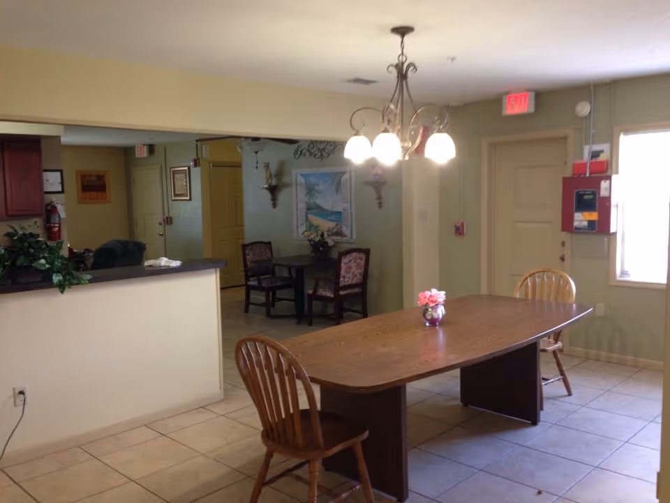 Senior living dining room with a long wooden table, chandelier, and pastel walls.
