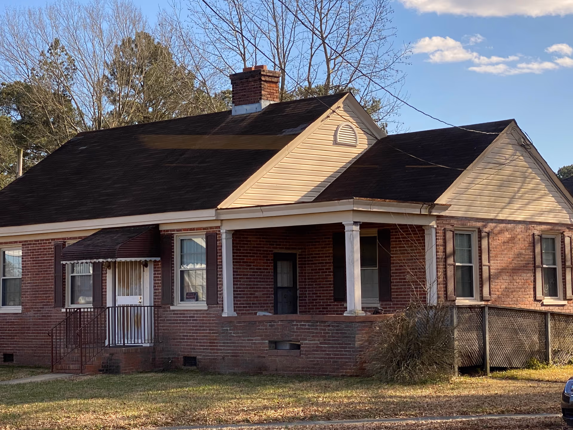 Brick single-story building with a front porch and white columns against a blue sky.