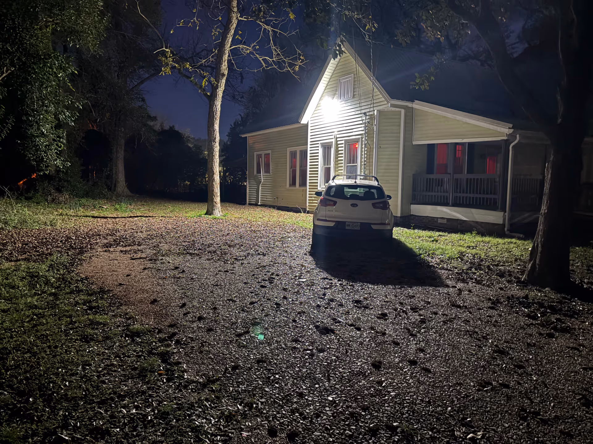 Night view of a beige single-story building with a car parked in front, trees nearby
