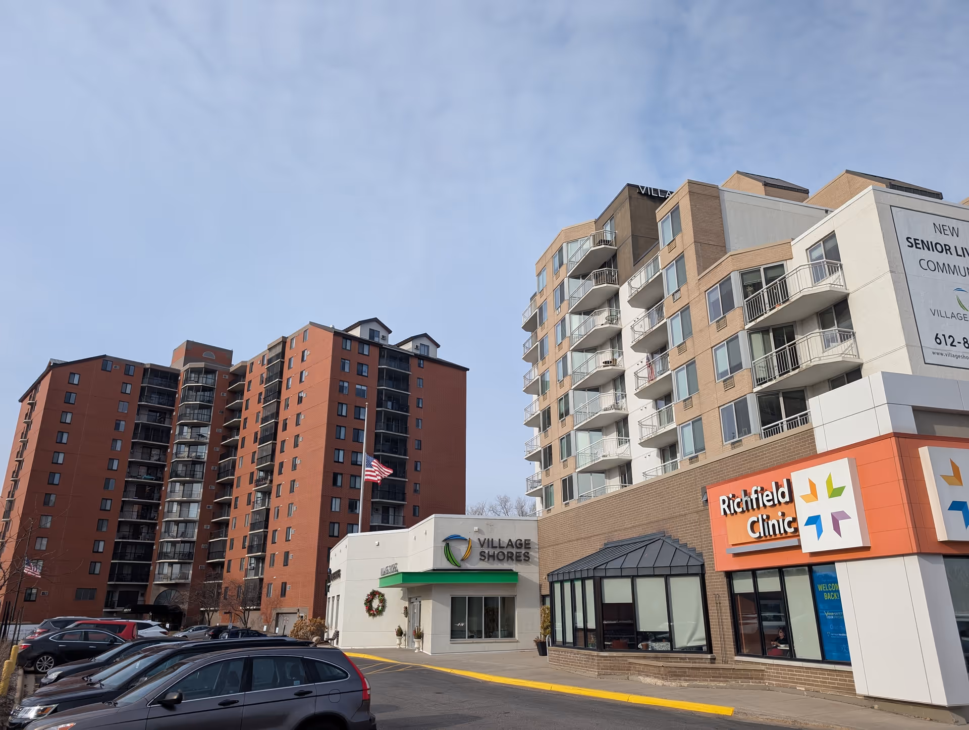 Exterior view of the Village Shores senior living building and adjacent Richfield Clinic with parked cars in the foreground.