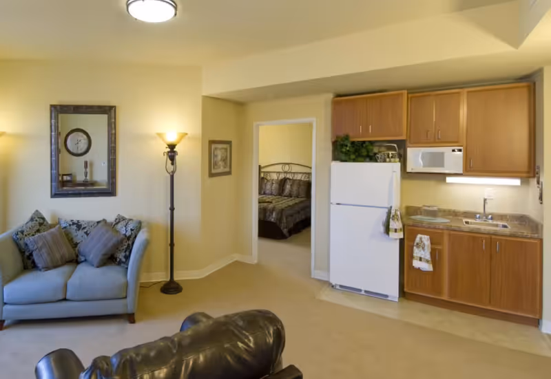 Living room area with sofa, floor lamp, and kitchenette in a compact suite.