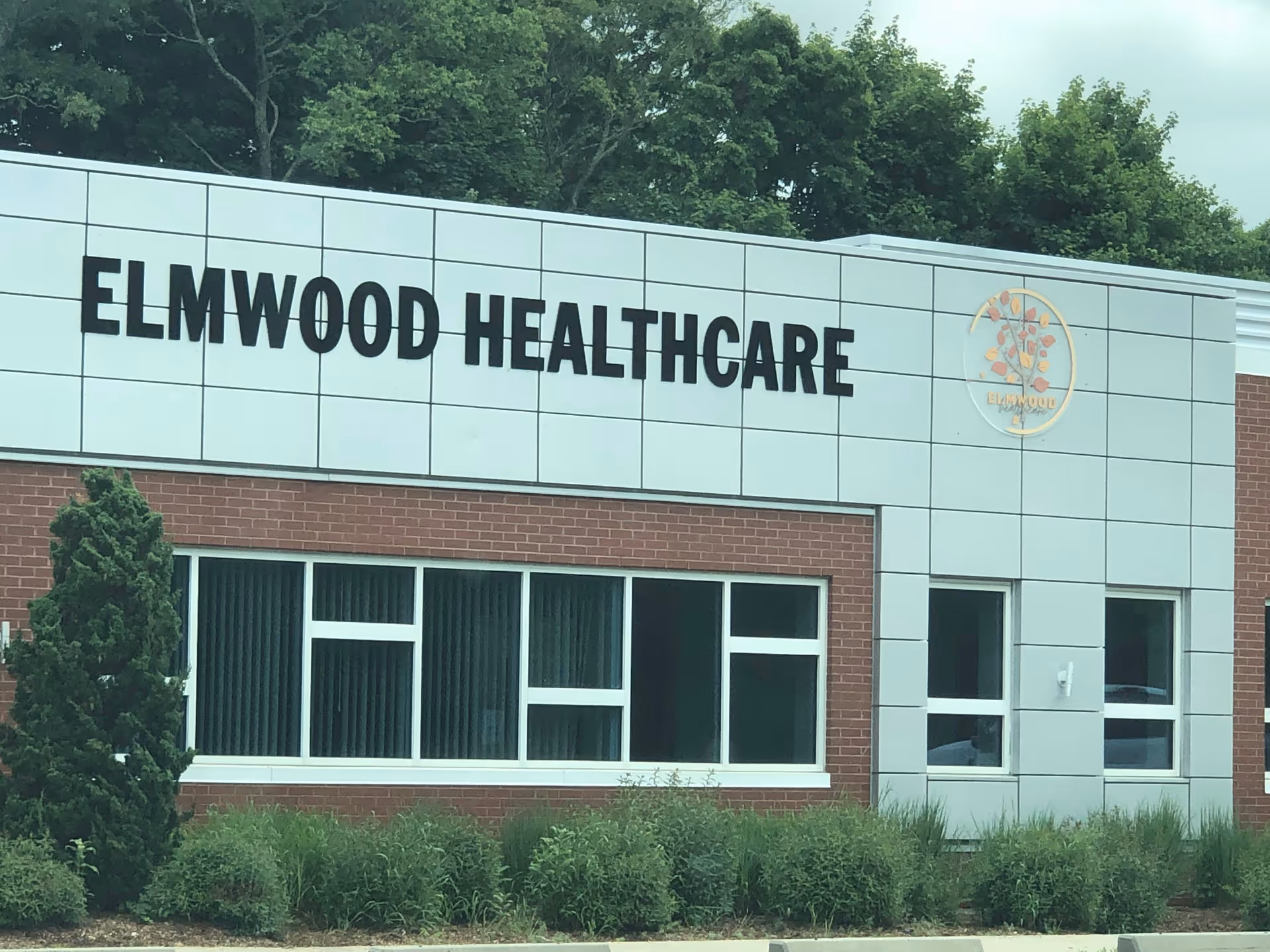 Exterior view of Elmwood Healthcare building with trees and shrubs.