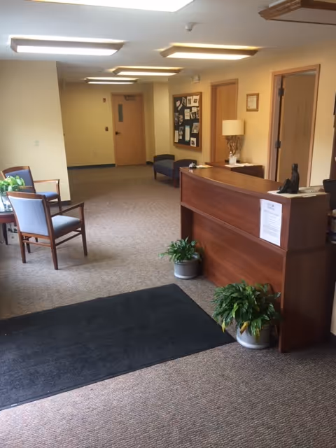 Facility lobby with a wooden reception desk, seating area, bulletin board, and potted plants.