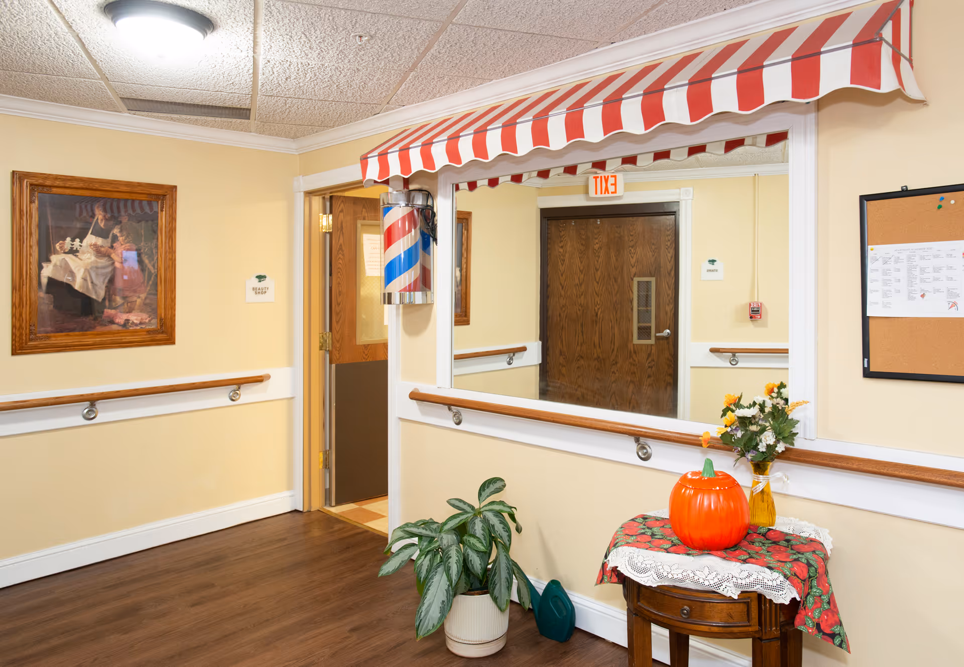 Interior hallway at Bayside Manor with striped awning, pumpkins, plants, mirror, and bulletin board.