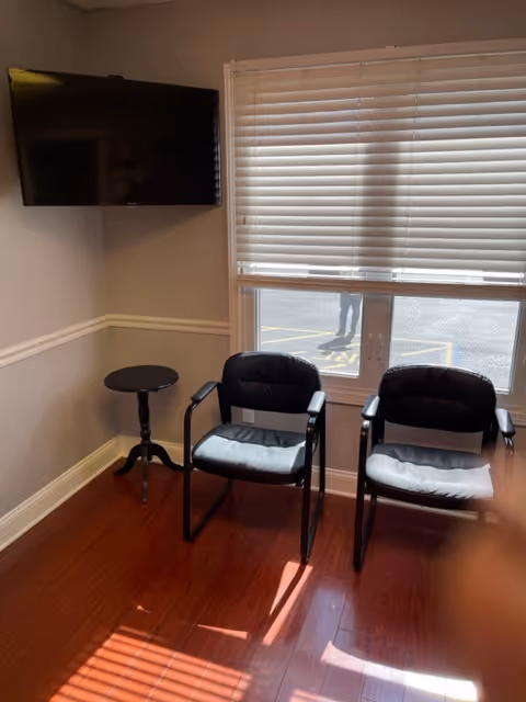 Two black chairs and a small round table sit in front of a window with blinds.