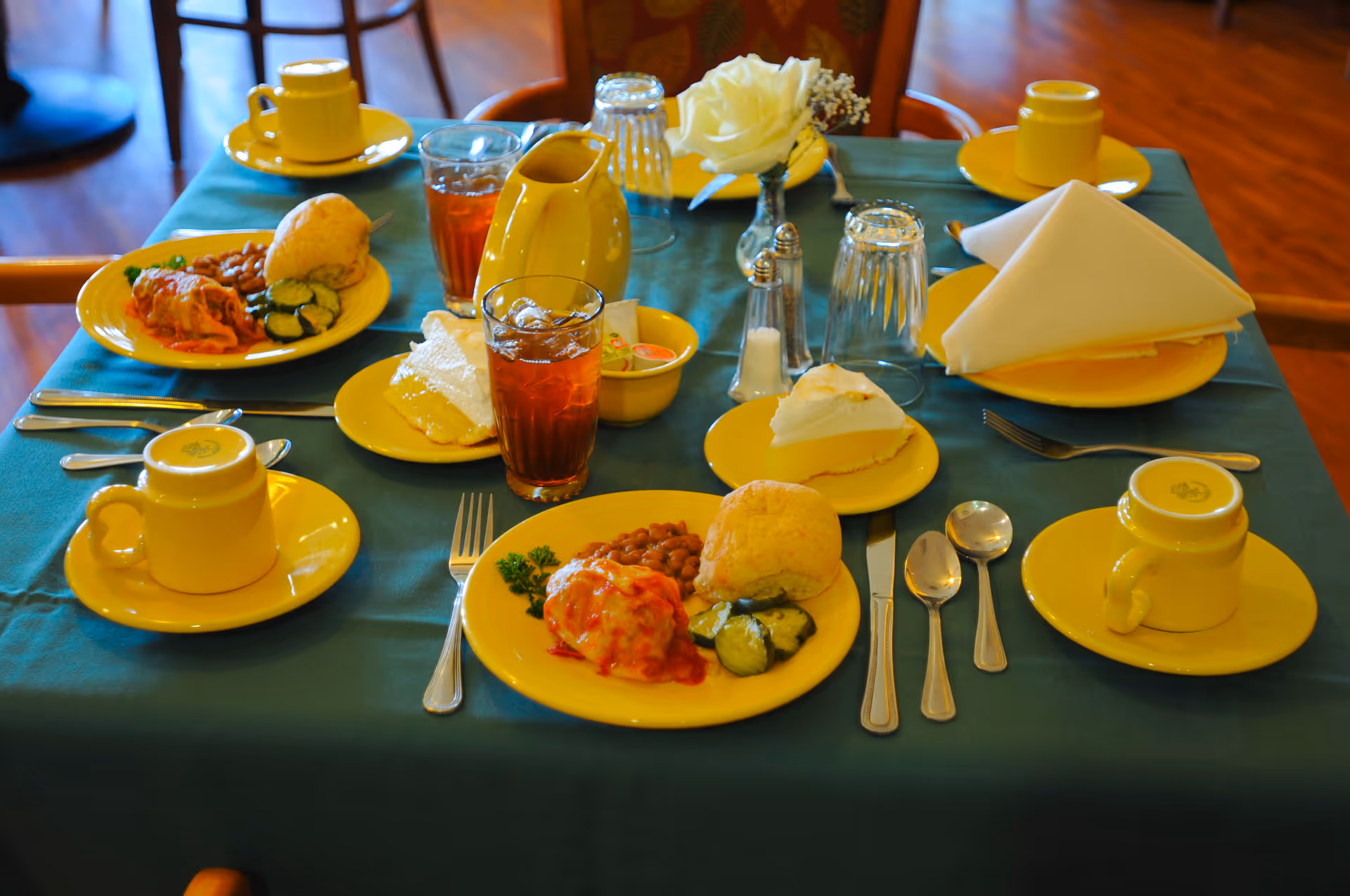 Table set for a meal with yellow dishes, cups, and food plates in dining room.