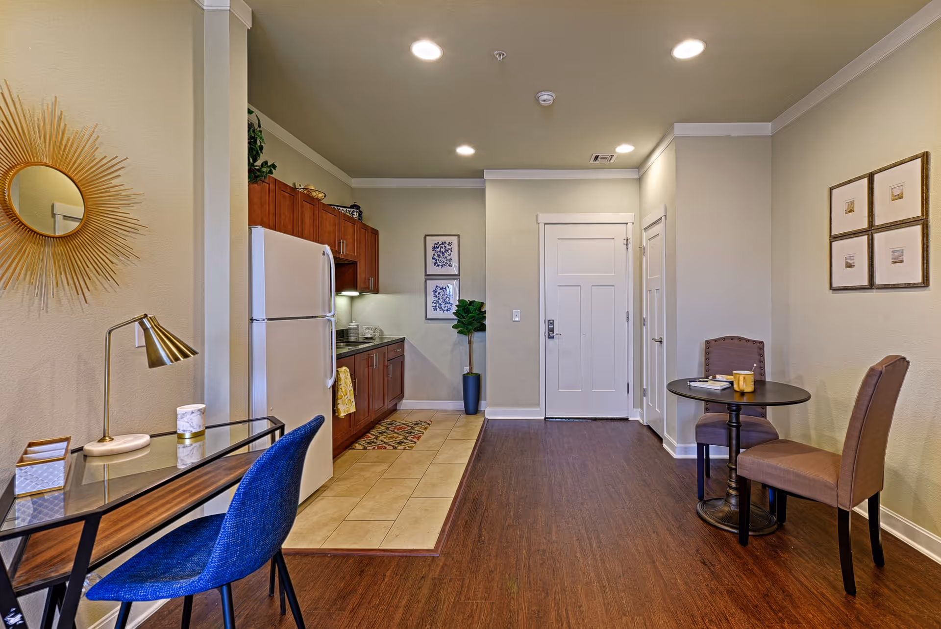 Furnished senior living common area with kitchenette, dining table, chairs, and entry door.