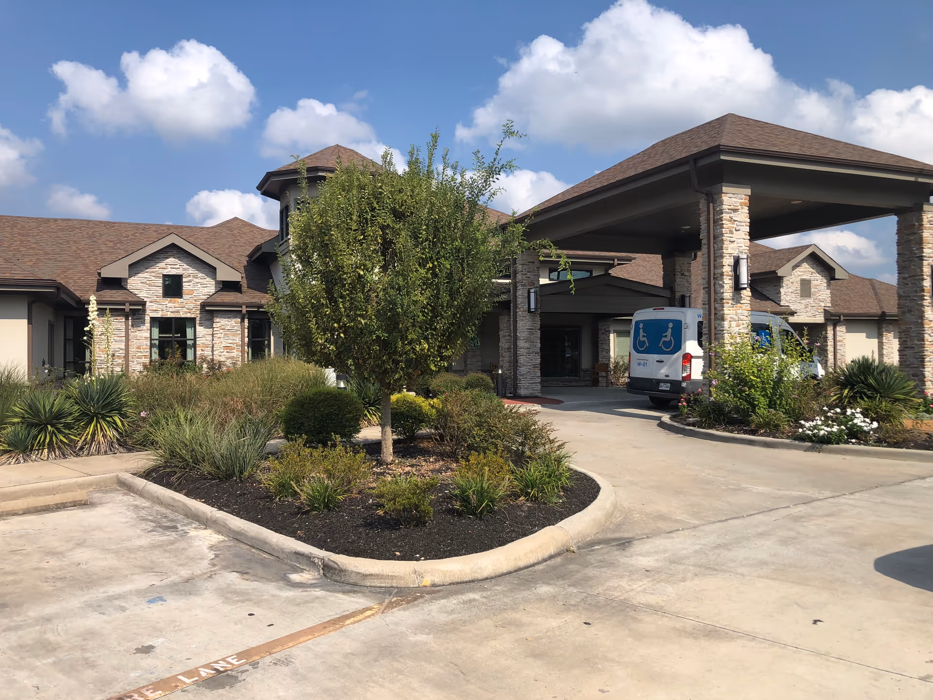 Front exterior of a senior living facility with landscaping and a wheelchair-accessible van.