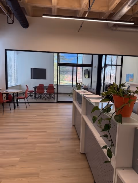 Interior view of a modern senior living common area with glass partition, red chairs, and plants.