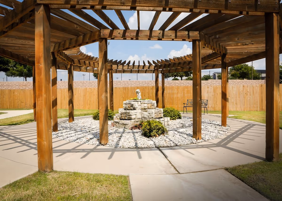 Wooden pergola shelters a stone fountain in a circular rock garden.
