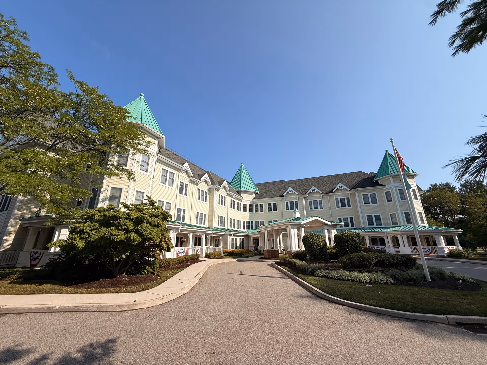 Cream-colored senior living building with green turret roofs, front entrance, and landscaped surroundings