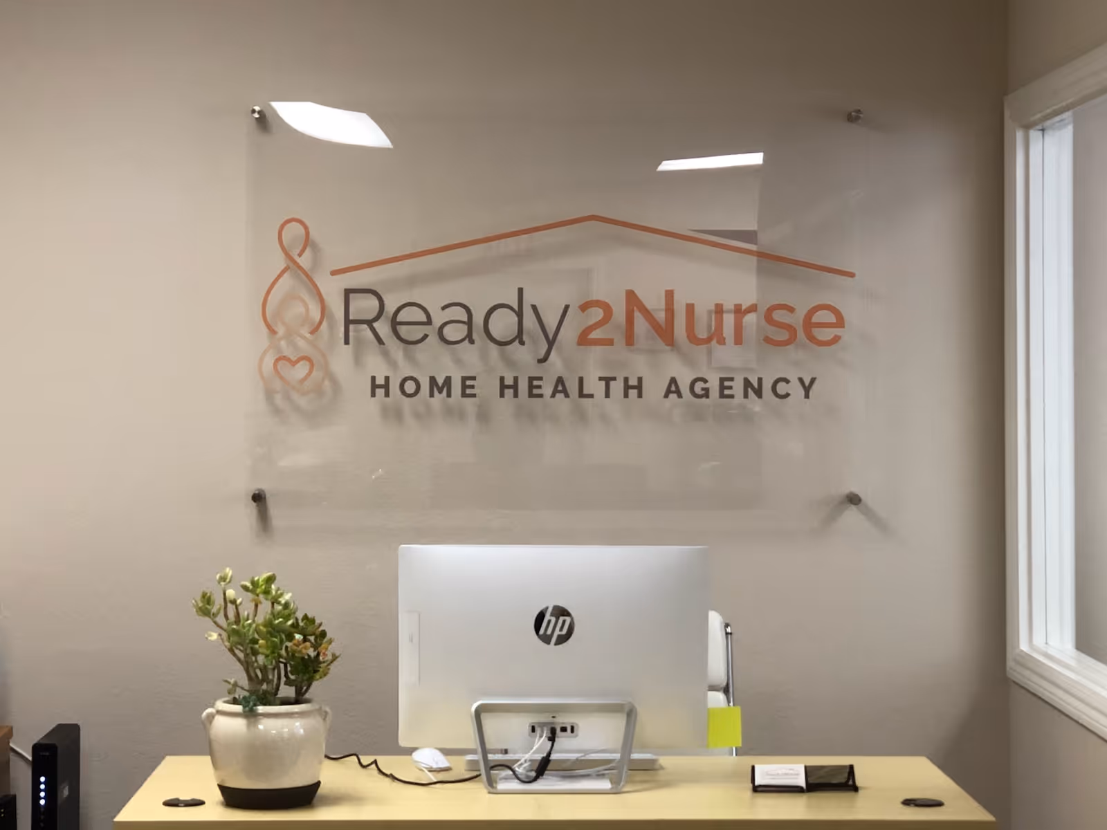 Reception desk with computer, plant, and Ready2Nurse sign on the wall.