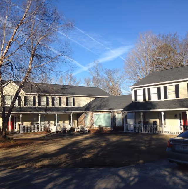 Two connected senior living buildings with porches, leafless trees, and a parked car.