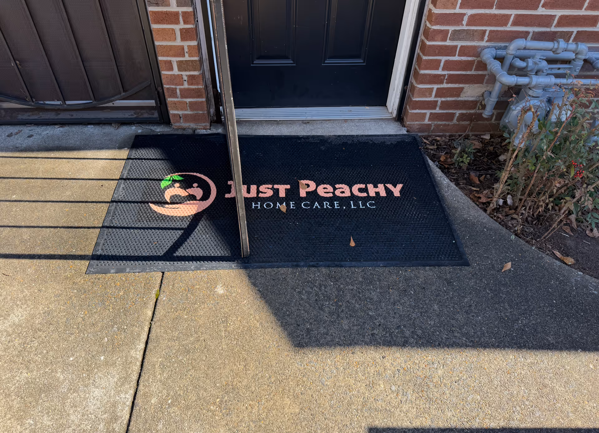 Entrance mat with Just Peachy Home Care logo on a brick building front.