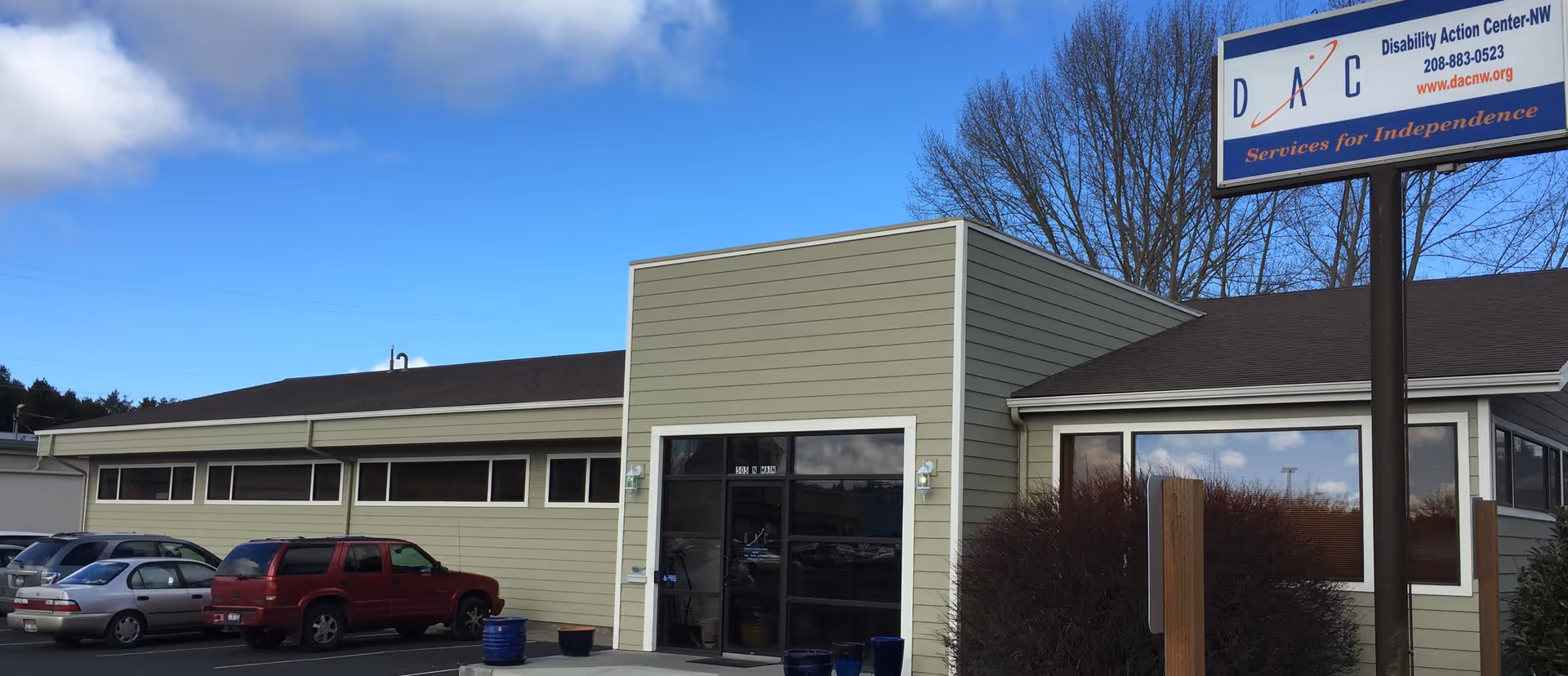Single story beige building with glass entrance and a parking lot under a clear blue sky.