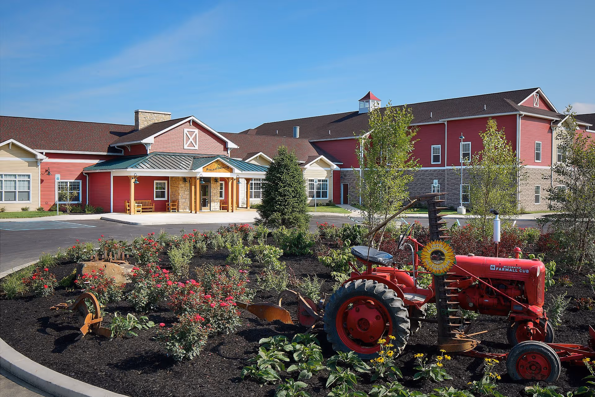 Front view of a red senior living facility with landscaped garden and vintage tractor.