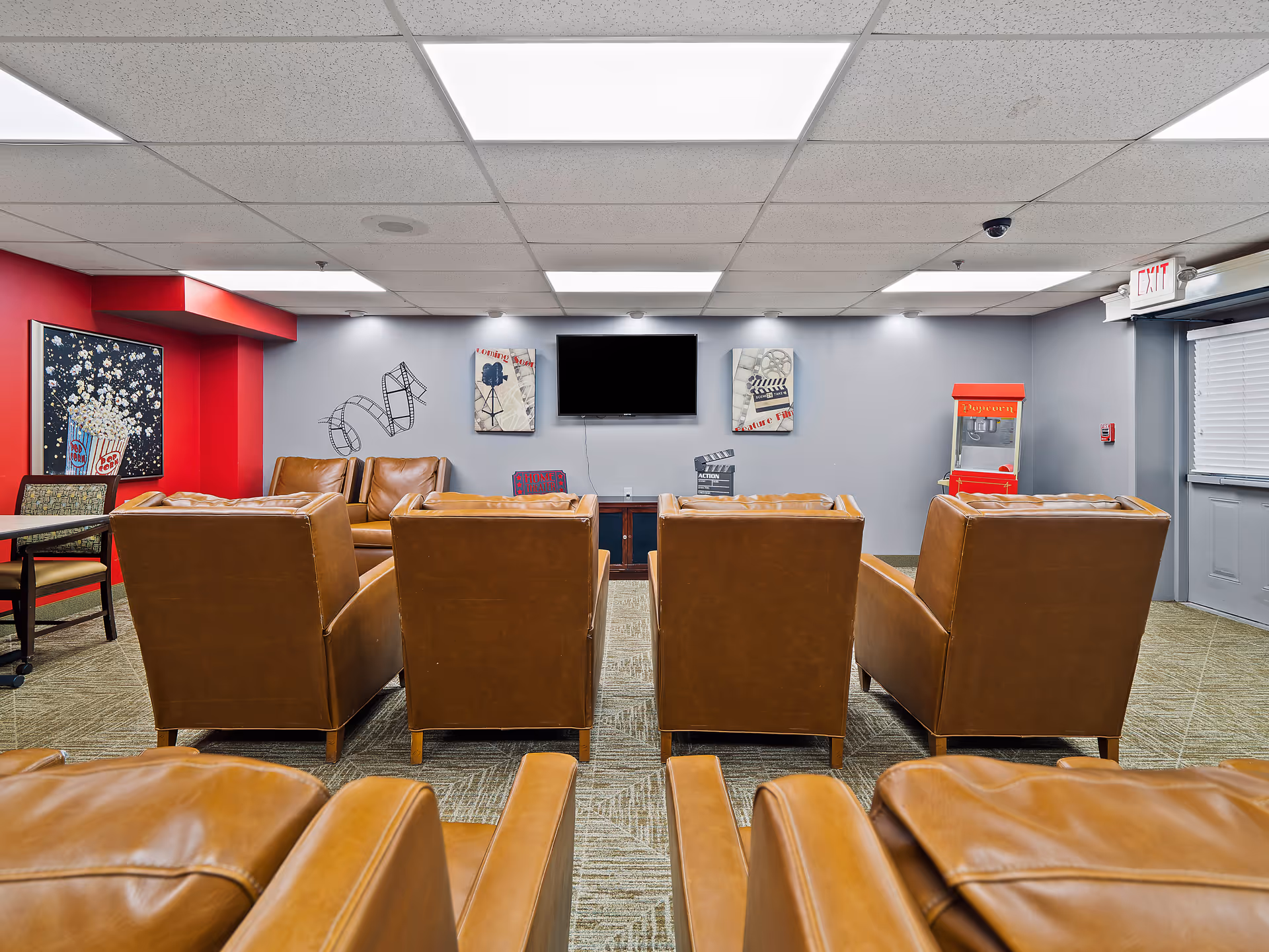 Senior living facility lounge with brown leather chairs facing a wall-mounted TV.