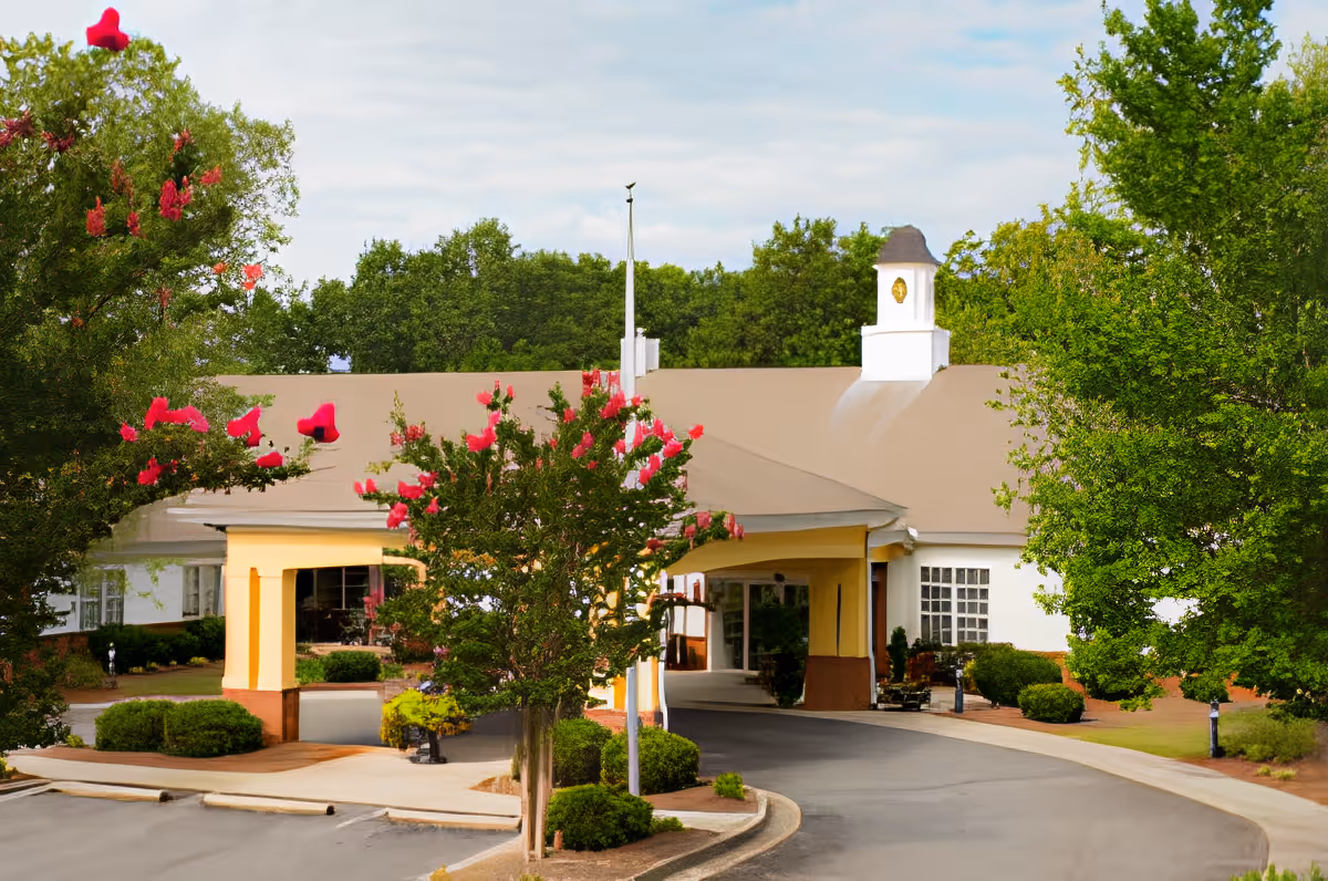 Front exterior view of TerraBella Marchbanks facility with a covered entrance, surrounded by trees and flowering bushes under a partly cloudy sky.