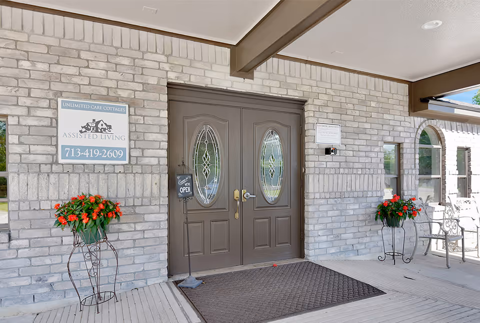 Brick exterior entrance with double doors, decorative glass, and two potted red flowers.