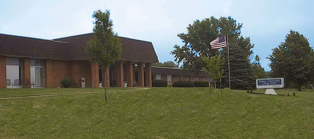 Exterior view of The Willows at Gretna with brick building, green lawn, trees, and flag.