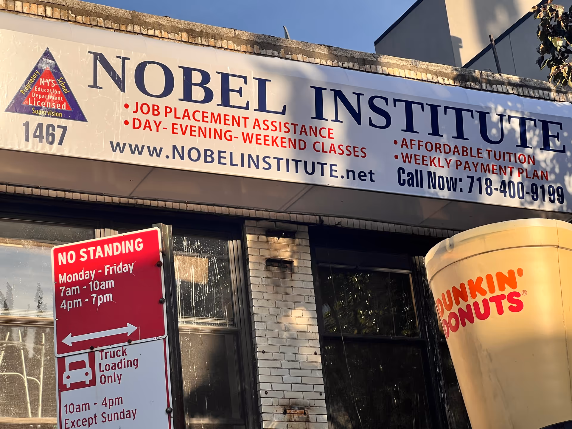 Exterior storefront displaying Nobel Institute sign, with a Dunkin' Donuts cup nearby.