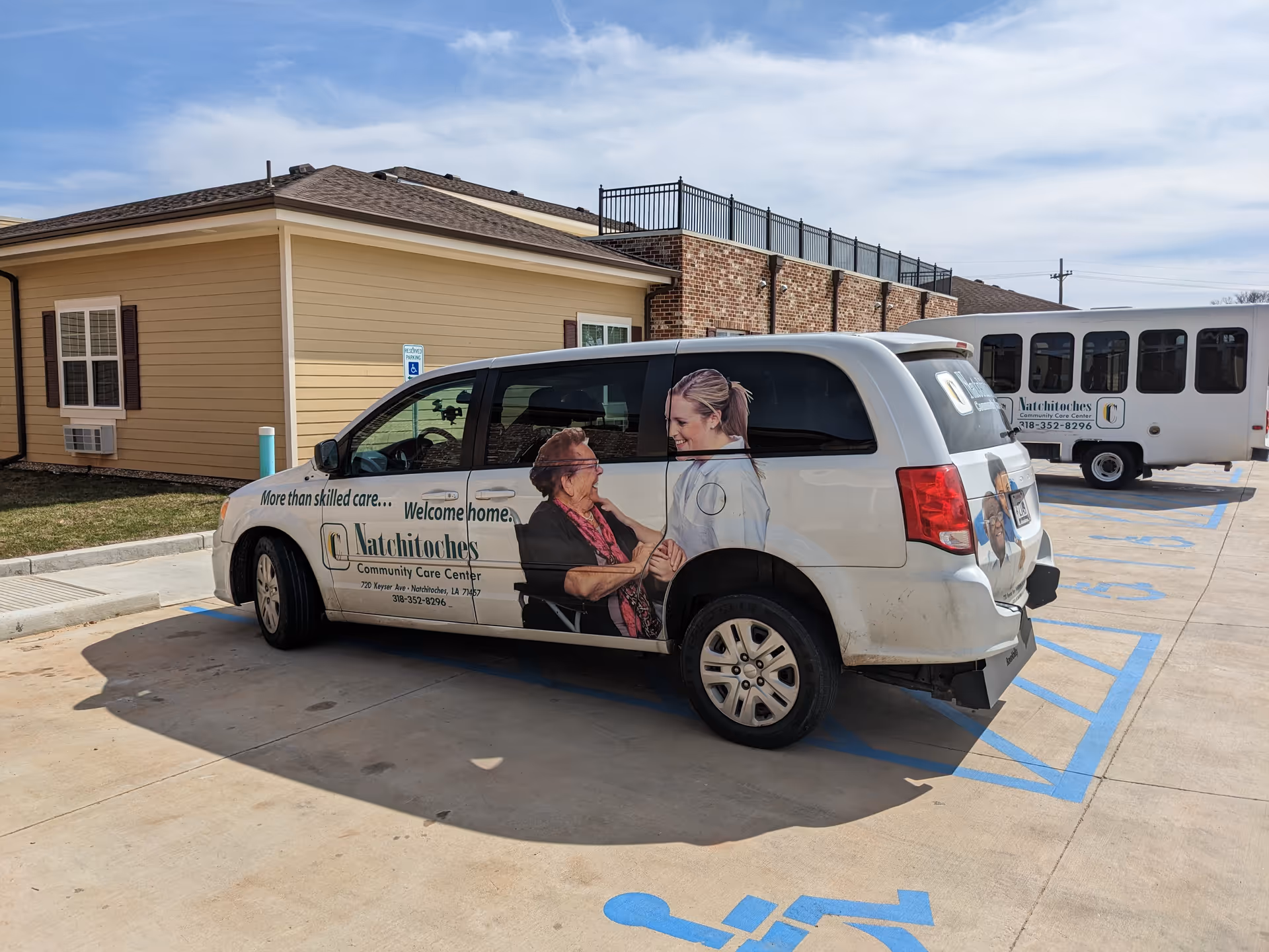 Exterior view of a tan facility with a branded care van in a handicap parking space.