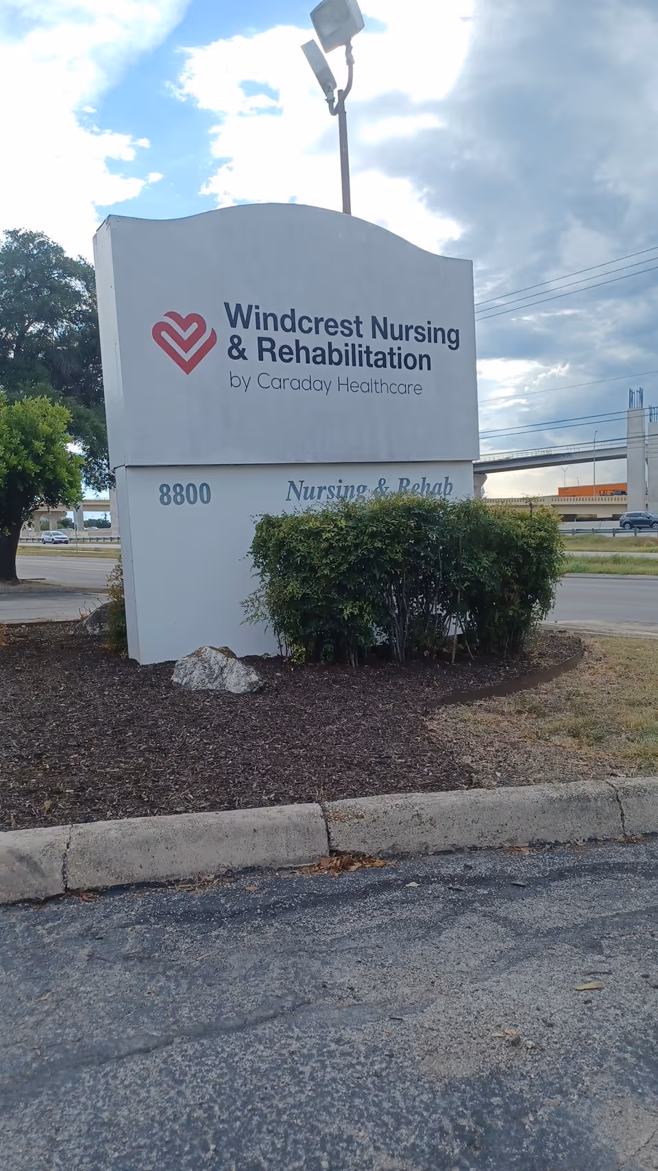 Exterior sign for Windcrest Nursing & Rehabilitation with landscaping in front.