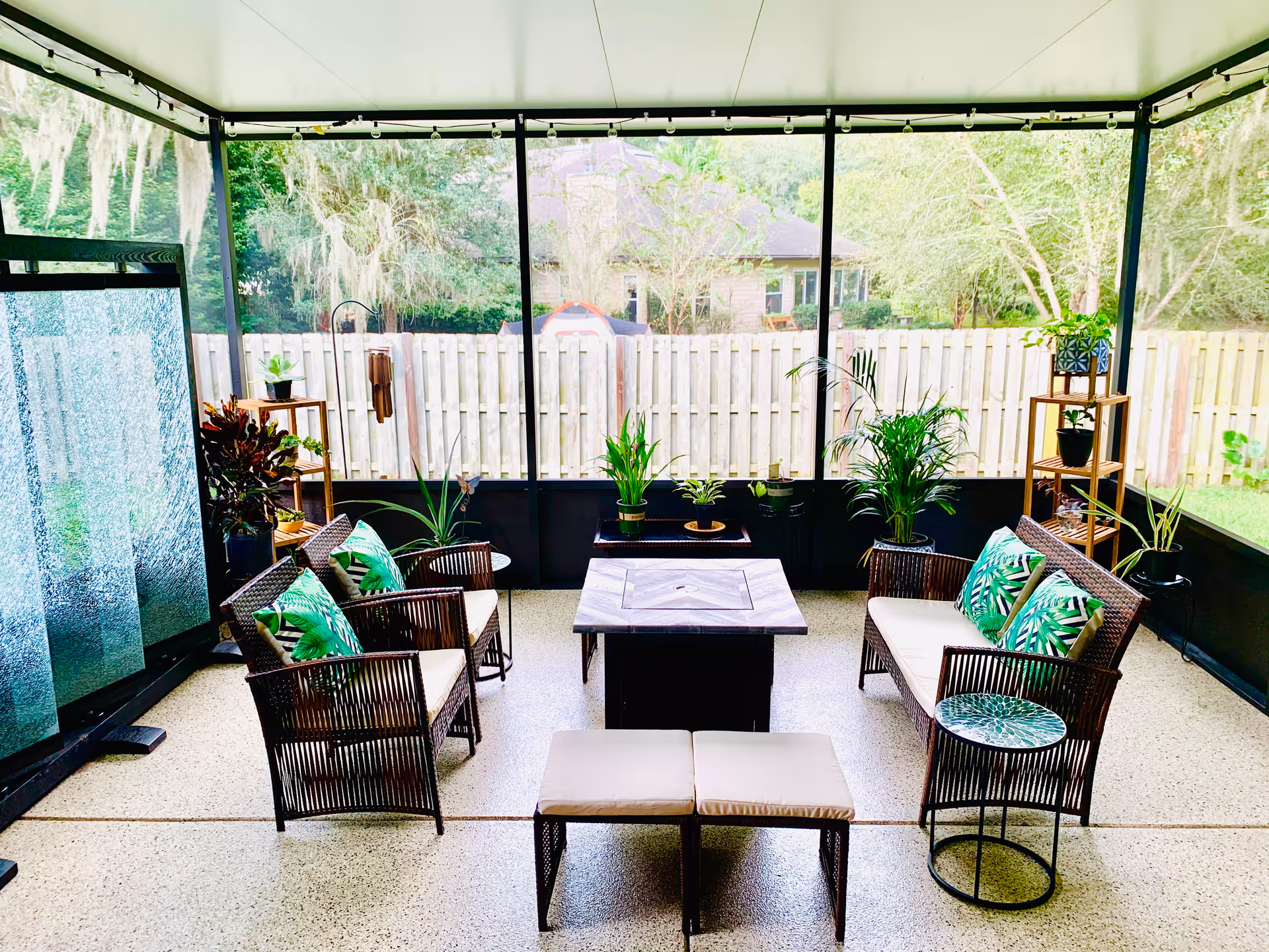 Screened outdoor seating area with wicker chairs, couches, and potted plants around a central table.