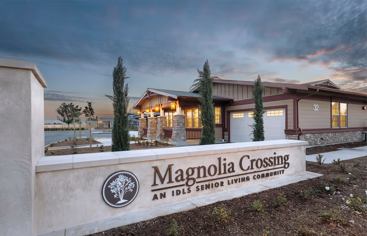 Exterior view of Magnolia Crossing assisted living facility with sign and entry driveway.