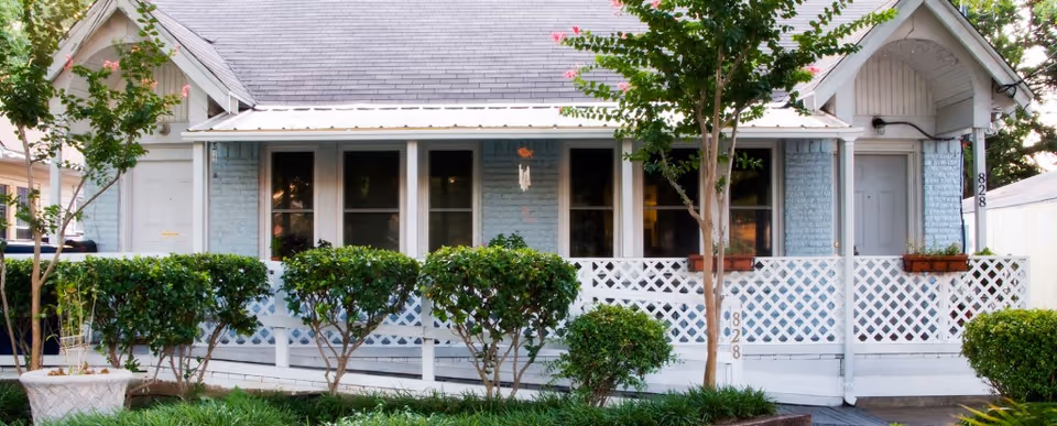 Front view of Legacy Cottage facility with white lattice porch and trimmed shrubs.