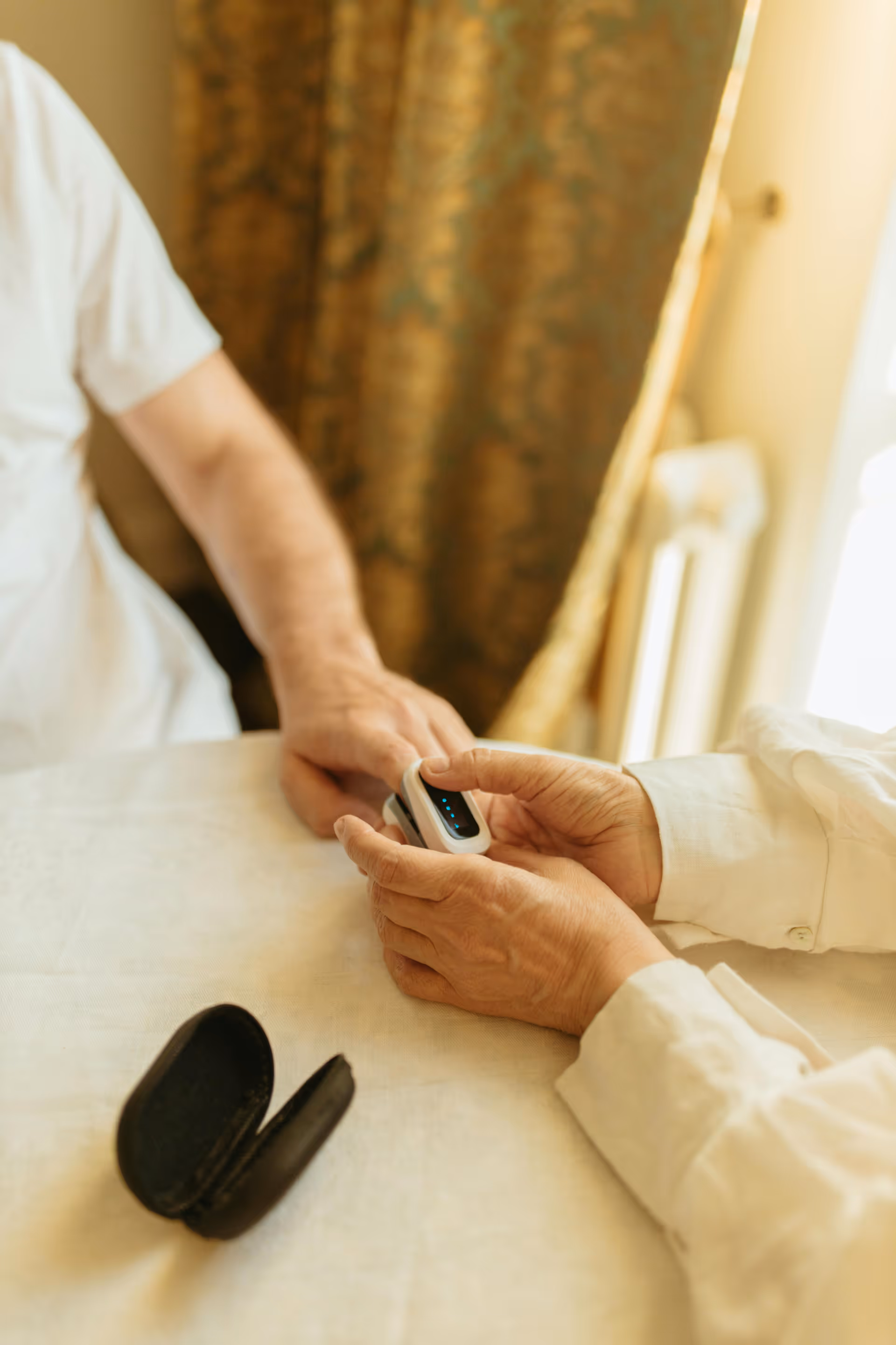 Two people use a small medical device at a bedside table.