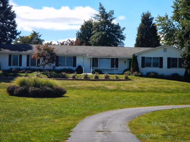 Front view of a single-story assisted living home with a curved driveway and lawn.