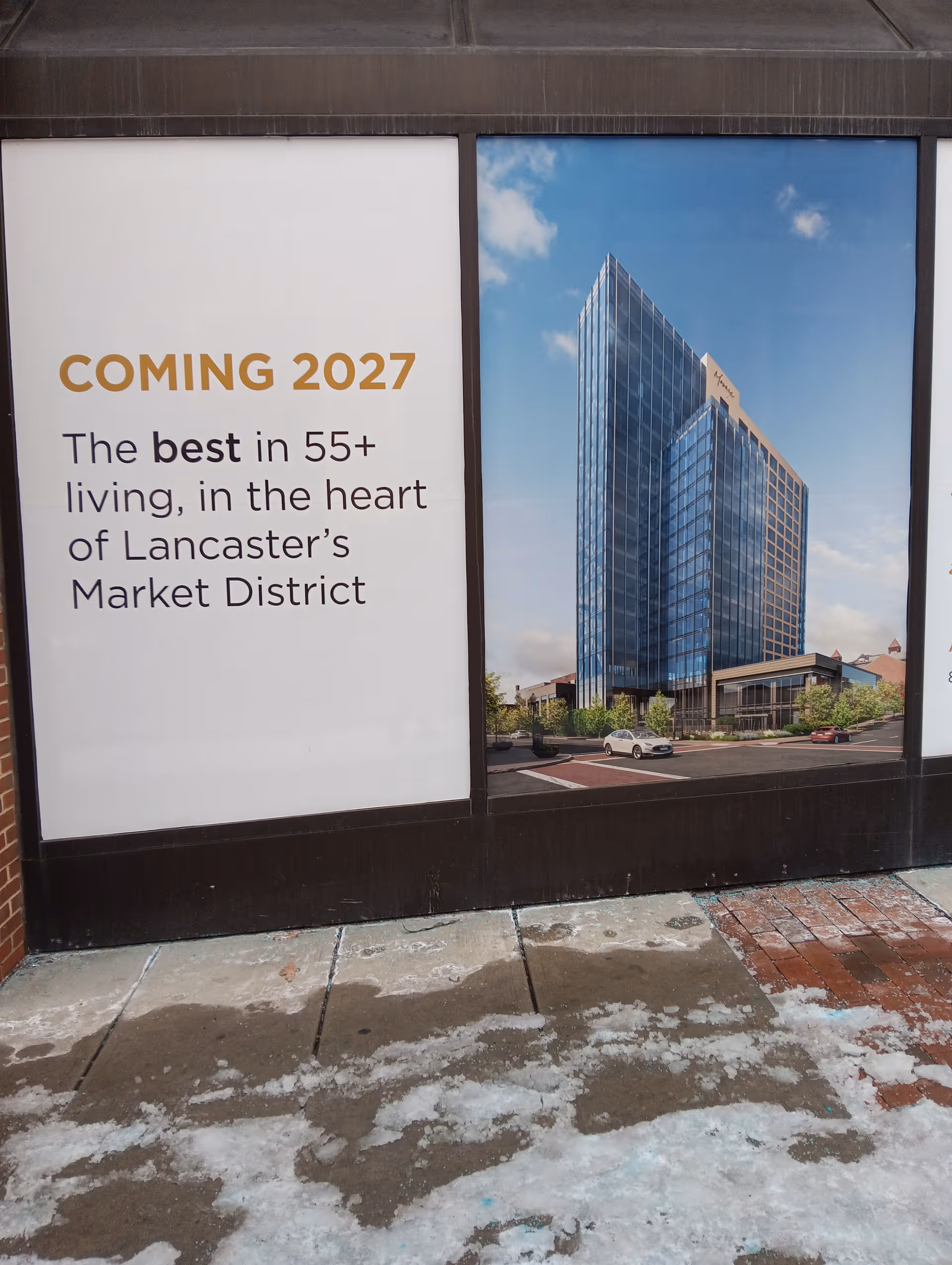 Storefront window displays advertisement panels promoting Coming 2027 for 55+ living.