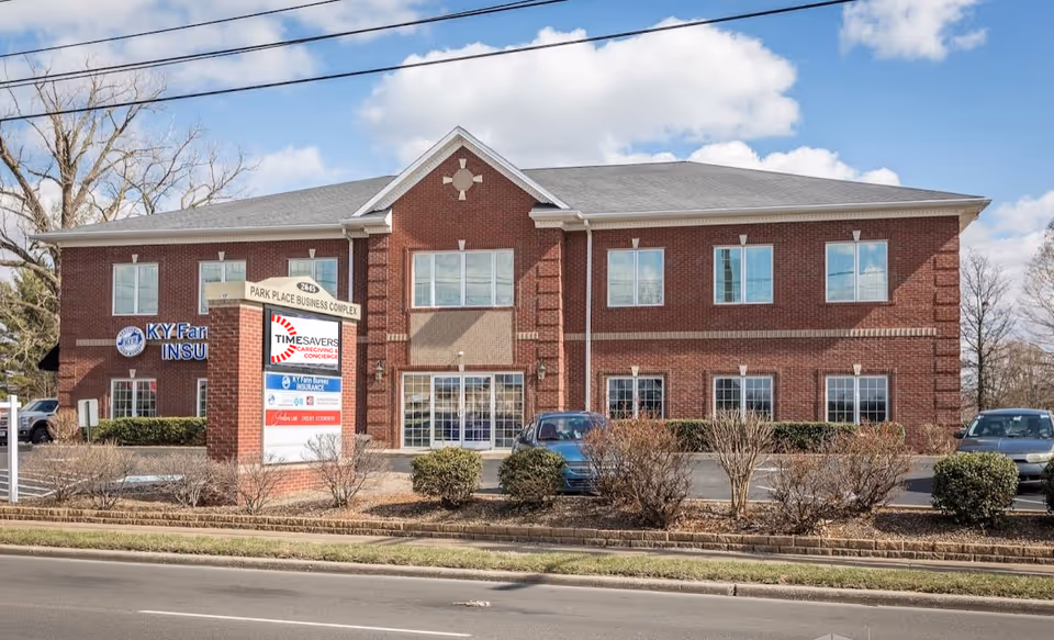 A brick two-story building labeled Timesavers Caregiving & Concierge, with parked cars in front.