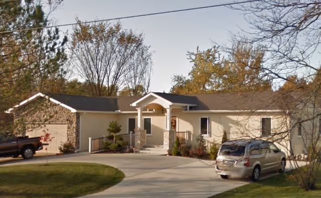 Single-story beige senior living facility with curved driveway, front entrance, and parked cars.